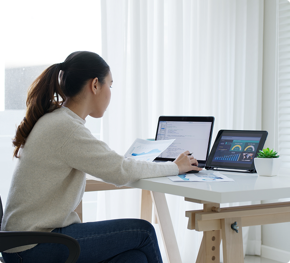 Professional working at desk with laptop and tablet displaying dashboards