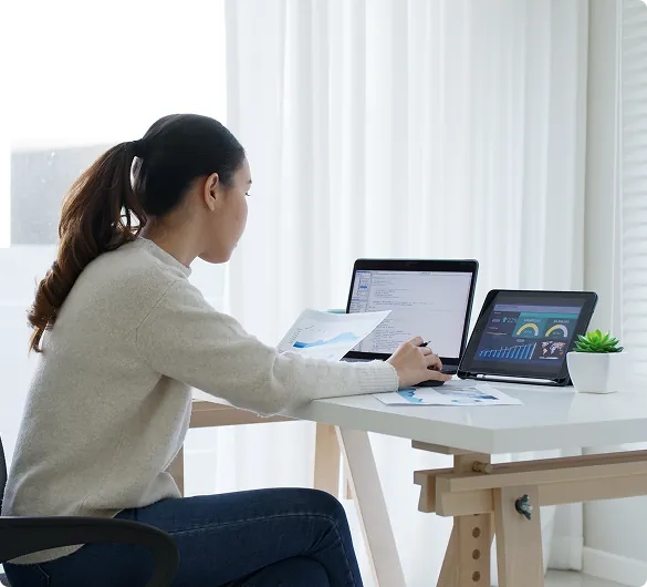 Professional working at desk with laptop and tablet displaying dashboards